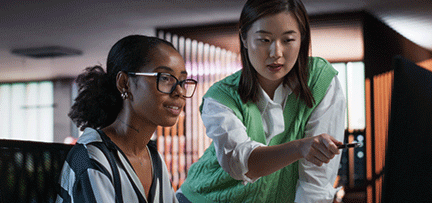 Two women in an office setting working at a computer 